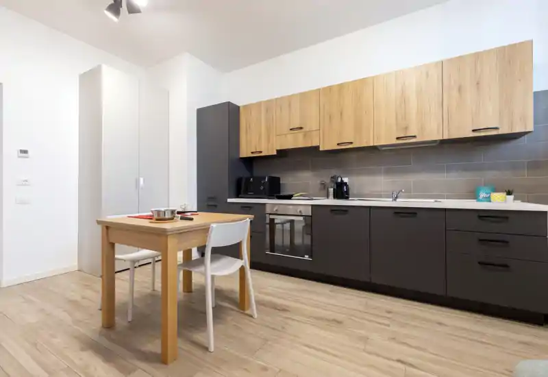 Modern fitted kitchen with wood upper cabinets and dark lower units, a built-in oven and a small wooden dining table—bright, clean and functional space ideal for apartment listings.