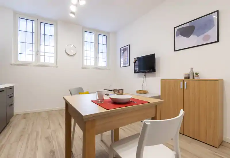 Compact, modern dining area with a wooden table set for a meal, bright windows and minimalist cabinetry—ideal for small apartments.