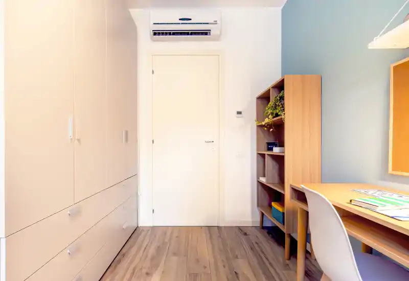 Small bedroom/bedroom corner with built-in wardrobe, desk and shelving; neat wooden floor and soft, neutral decor. The image focuses on storage and workspace rather than a bed.