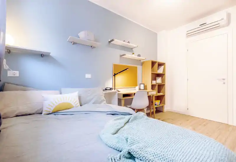 Camera da letto luminosa e accogliente con un grande letto in primo piano, morbidi tessuti e un angolo studio ordinato con scrivania e scaffali.