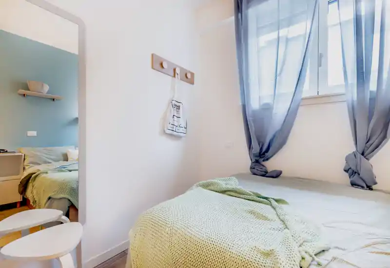 Camera da letto luminosa e curata con un letto confortevole coperto da una coperta testurizzata e luce naturale dalla finestra; toni neutri e arredo minimale creano un ambiente tranquillo, ideale per gli annunci.