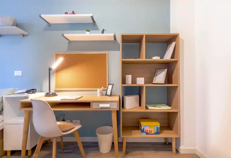 Angolo studio ben arredato con scrivania in legno, sedia e scaffalatura a vista. La lampada da tavolo calda e gli accessori ordinati creano un'area di lavoro accogliente, perfetta per un annuncio.