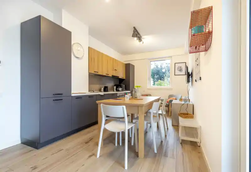 Modern open kitchen with integrated cabinets and a wooden dining table for four; bright, tidy and tastefully decorated, ideal for apartment listings highlighting a functional kitchen-diner.