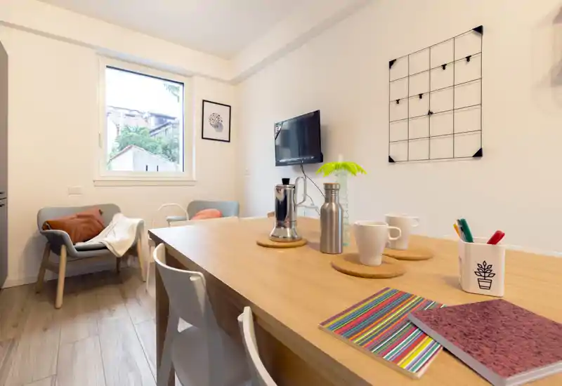 Bright, modern dining area with a wooden table set for casual use. Two chairs and cozy armchairs by the window create a welcoming nook perfect for meals or remote work.