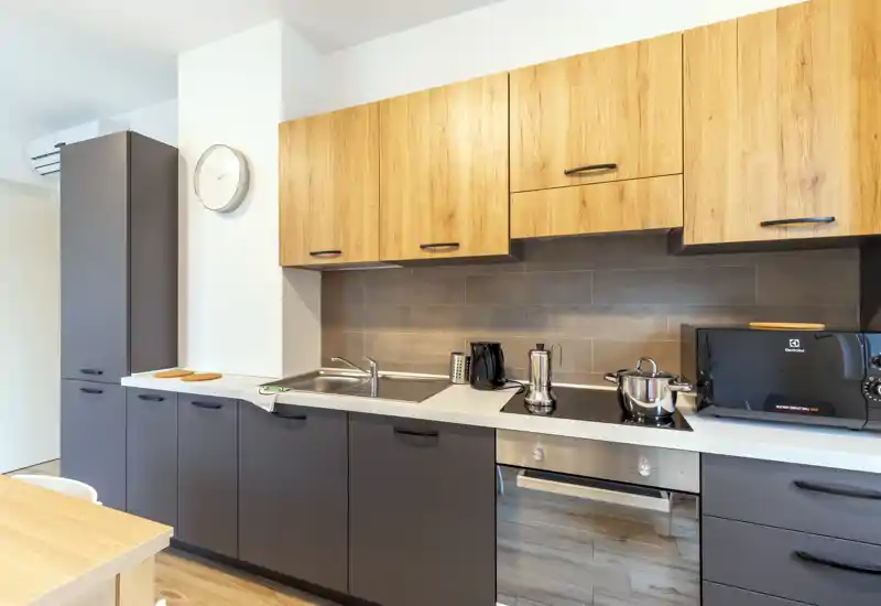Modern fitted kitchen with matte gray lower cabinets and warm wood upper cabinets, equipped with a sink, induction hob, oven and countertop appliances—bright, clean and ready for use.