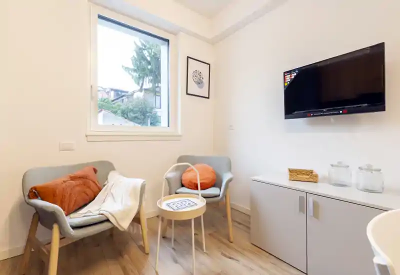 Small, bright living area with two upholstered armchairs, a side table and wall-mounted TV. Neutral decor, wooden flooring and soft textiles create a welcoming, modern sitting corner ideal for relaxation.