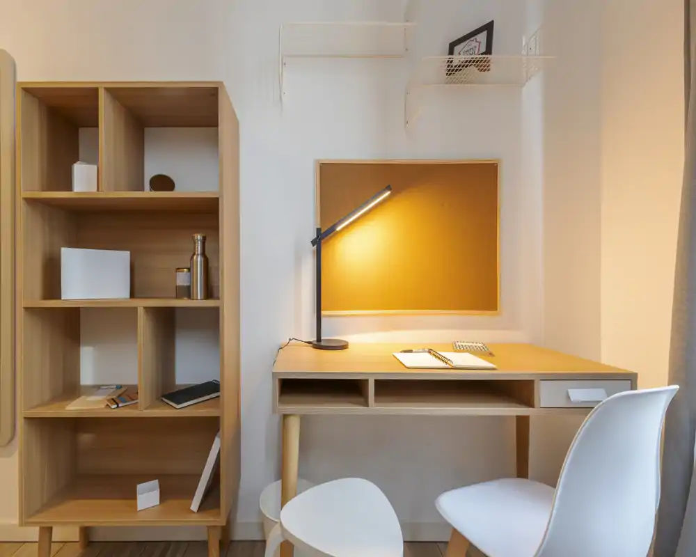 Angolo studio ordinato e minimale con scrivania in legno, lampada e scaffalatura — perfetto per lavorare o leggere in un appartamento compatto.