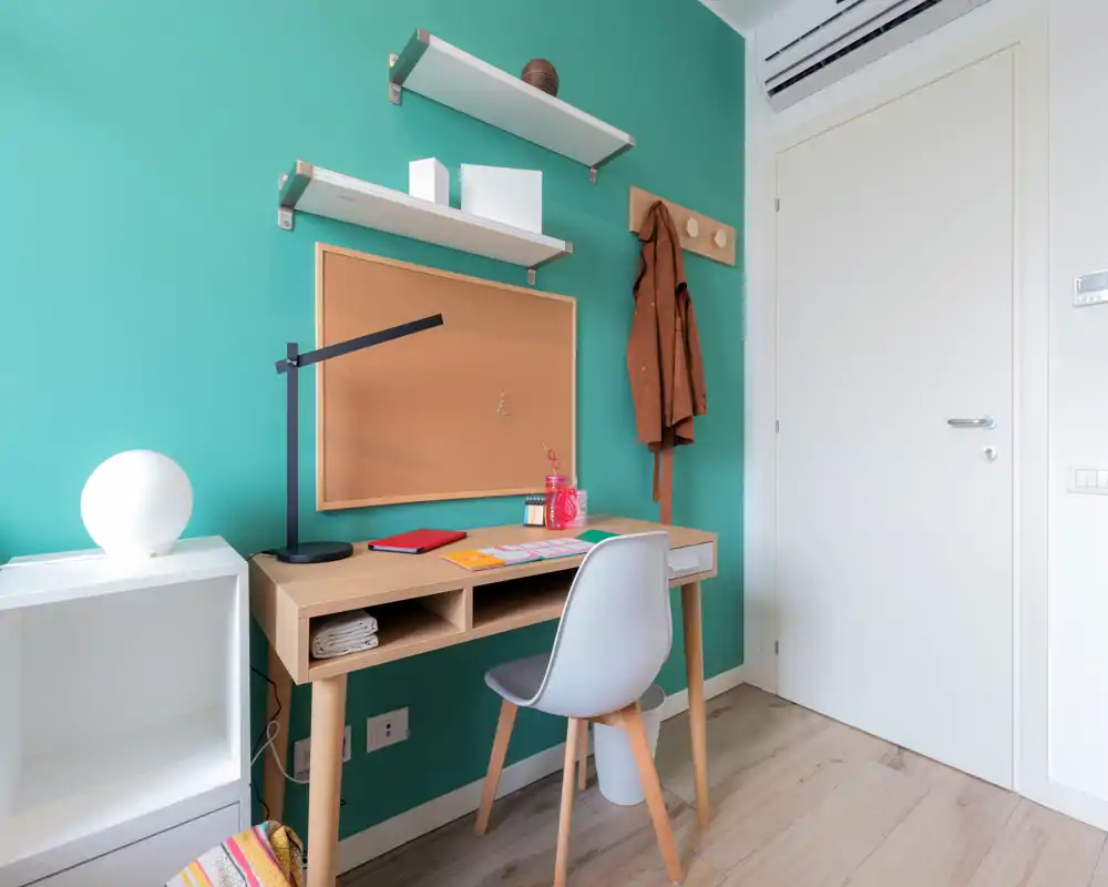 Bright, modern study corner with a wooden desk, ergonomic chair and cork noticeboard against a teal accent wall — ideal for working or studying.