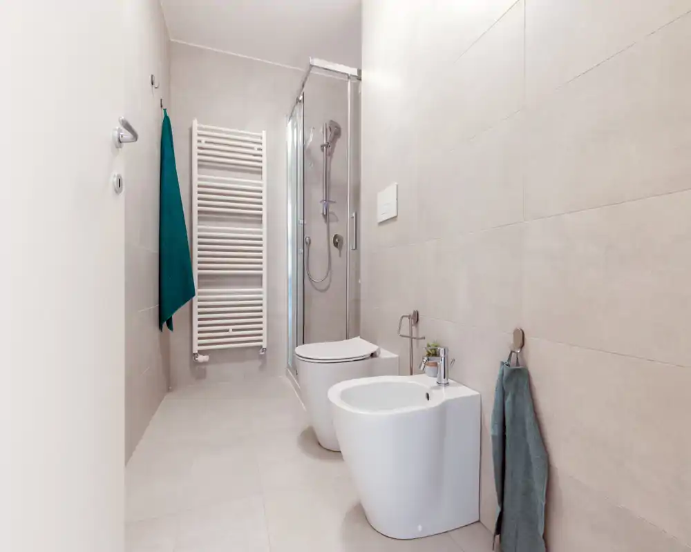 Modern, compact bathroom with a shower cabin, wall-mounted toilet and bidet, neutral tiles and tidy accessories.