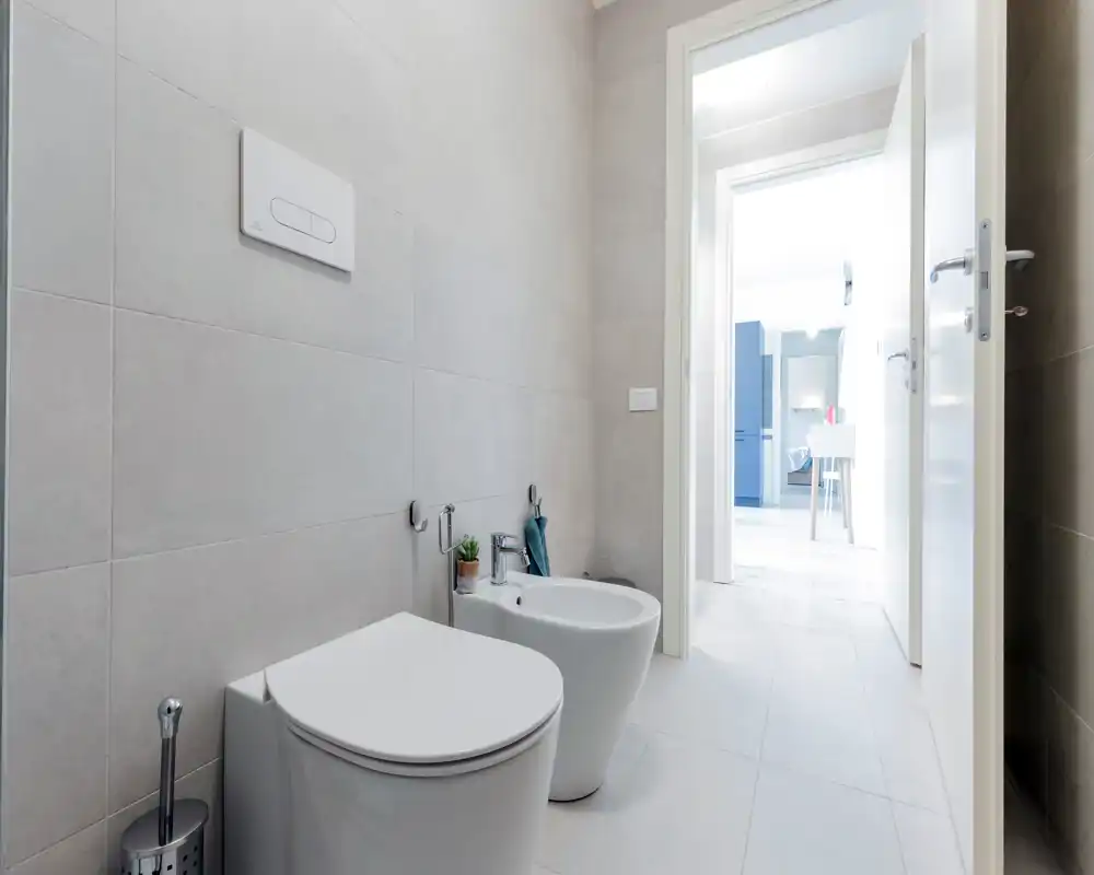 Modern, bright bathroom featuring a wall-mounted toilet and bidet, light grey tiles and clean minimalist fixtures.