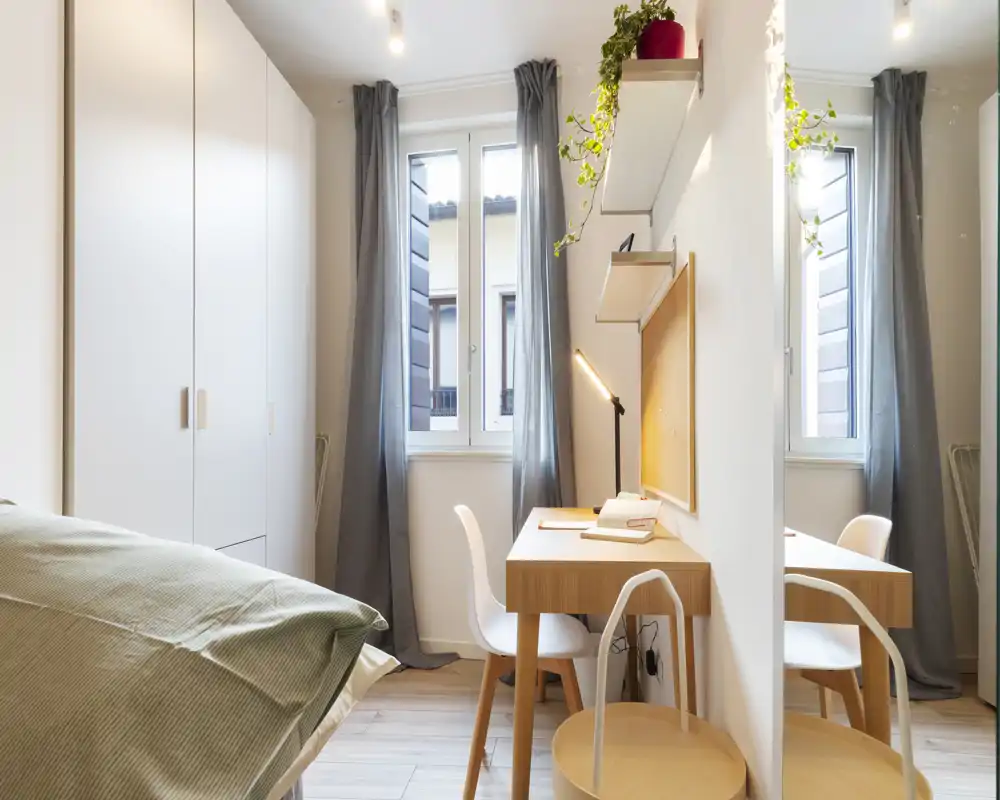Chambre moderne et lumineuse avec lit bien fait, placard intégré et bureau compact près de la fenêtre — idéal pour travailler et se détendre dans un espace bien éclairé.