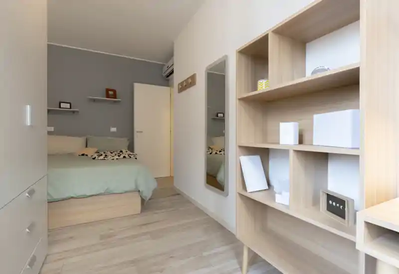 Bright, modern bedroom with a double bed dressed in soft linens, minimalist shelving and a light wood shelving unit creating a calm, airy atmosphere.