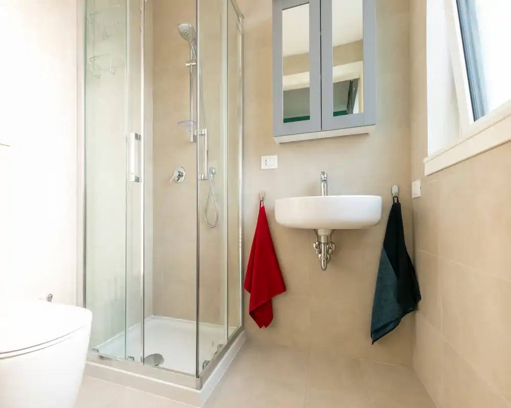 Bright, modern bathroom with a glass-enclosed shower, wall-mounted sink and neutral tile finish — clean and minimal.