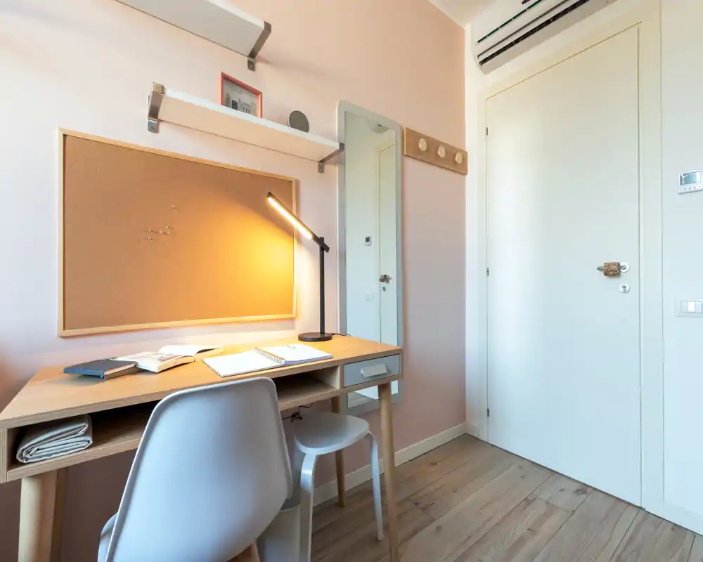 Bright, stylish home office corner with a wooden desk, chair and warm desk lamp against a pastel wall — ideal for studying or remote work.