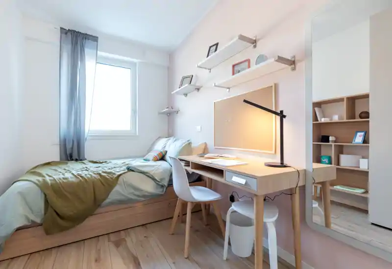 Bright, neatly styled single bedroom with a wooden platform bed, study desk and shelving—ideal for a student or solo tenant.