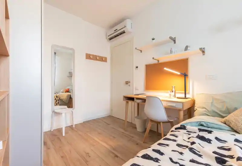 Well-lit bedroom corner with a visible single bed, bedside cushions and a compact study desk with a lamp — tidy and welcoming for a rental listing.
