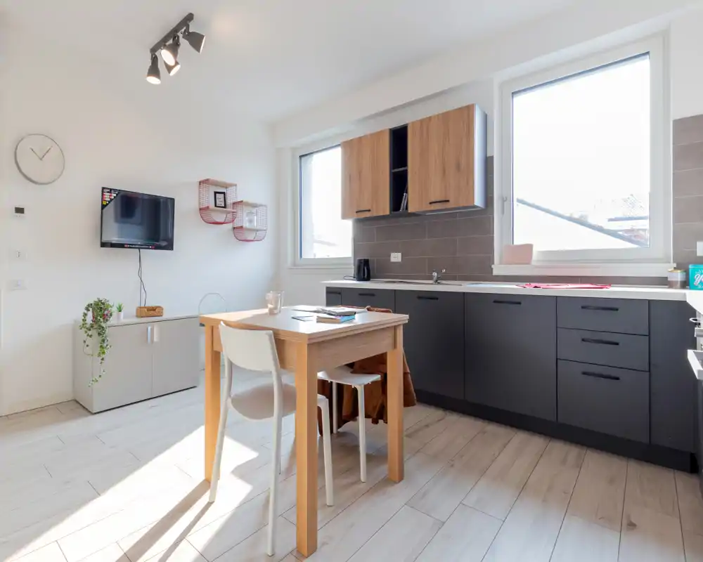 Bright modern kitchen with matte dark lower cabinets, wood upper cabinets and a small dining table bathed in natural light — ideal for compact apartment listings.