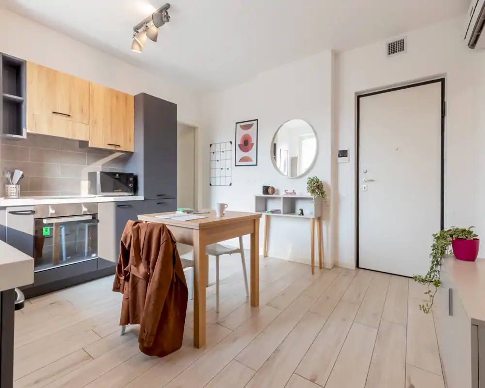 Bright, modern open-plan kitchen with wood-accent cabinets, integrated oven and a small dining table — nicely staged with plants and wall decor.