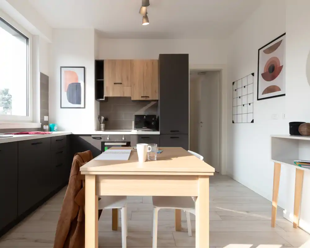 Bright modern kitchen with a wooden dining table, integrated dark cabinets and warm wood accents; large window provides abundant natural light.