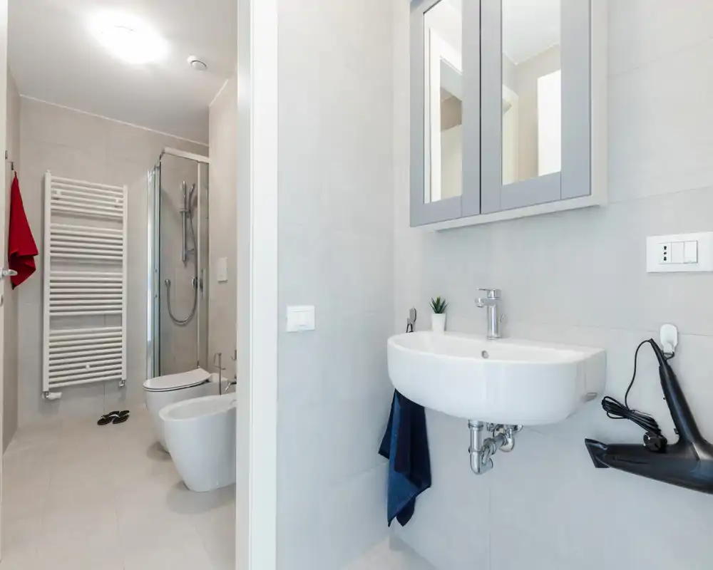 Bright, modern bathroom with wall-mounted sink, mirrored cabinet, bidet, toilet and enclosed shower — clean minimalist design and neutral tiles.
