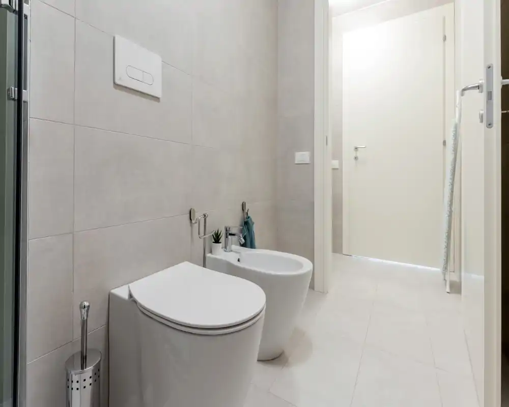 Modern, bright bathroom with a wall-mounted toilet and bidet, light tiles and a clean minimalist finish.