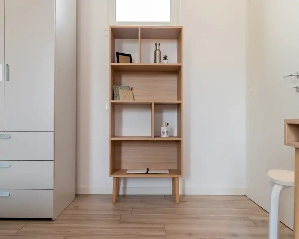 Minimal bedroom corner with a light wood shelving unit, wardrobe and bright natural light; simple, modern styling suitable for a tidy rental listing.