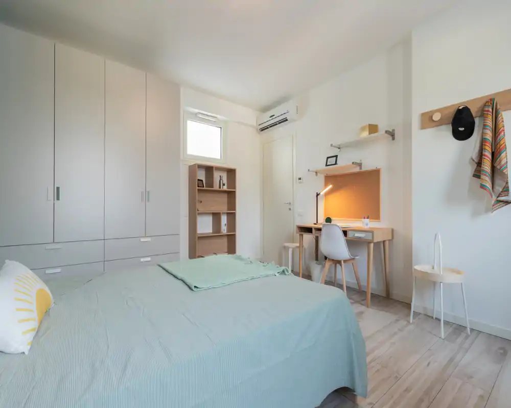 Bright, modern bedroom with a neatly made bed, built-in wardrobe and a compact study desk — ideal for students or professionals seeking a minimalist, well-lit room.