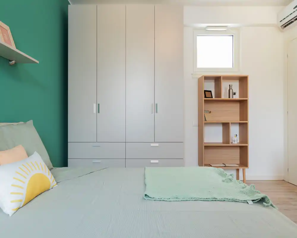 Bright modern bedroom with a mint-green accent wall, large wardrobe and a neatly made bed with decorative cushions and a light throw — comfortable and photo-ready.