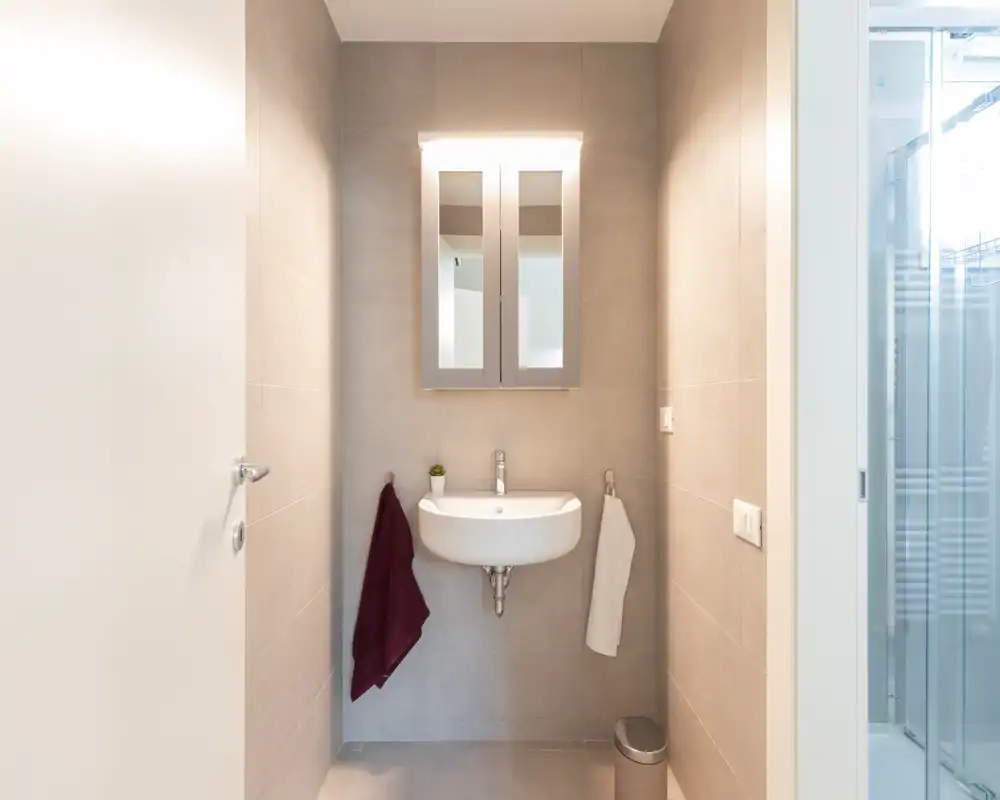 Compact, modern bathroom with wall-mounted sink, mirrored medicine cabinet and a bright, tiled finish ideal for an ensuite or guest washroom.
