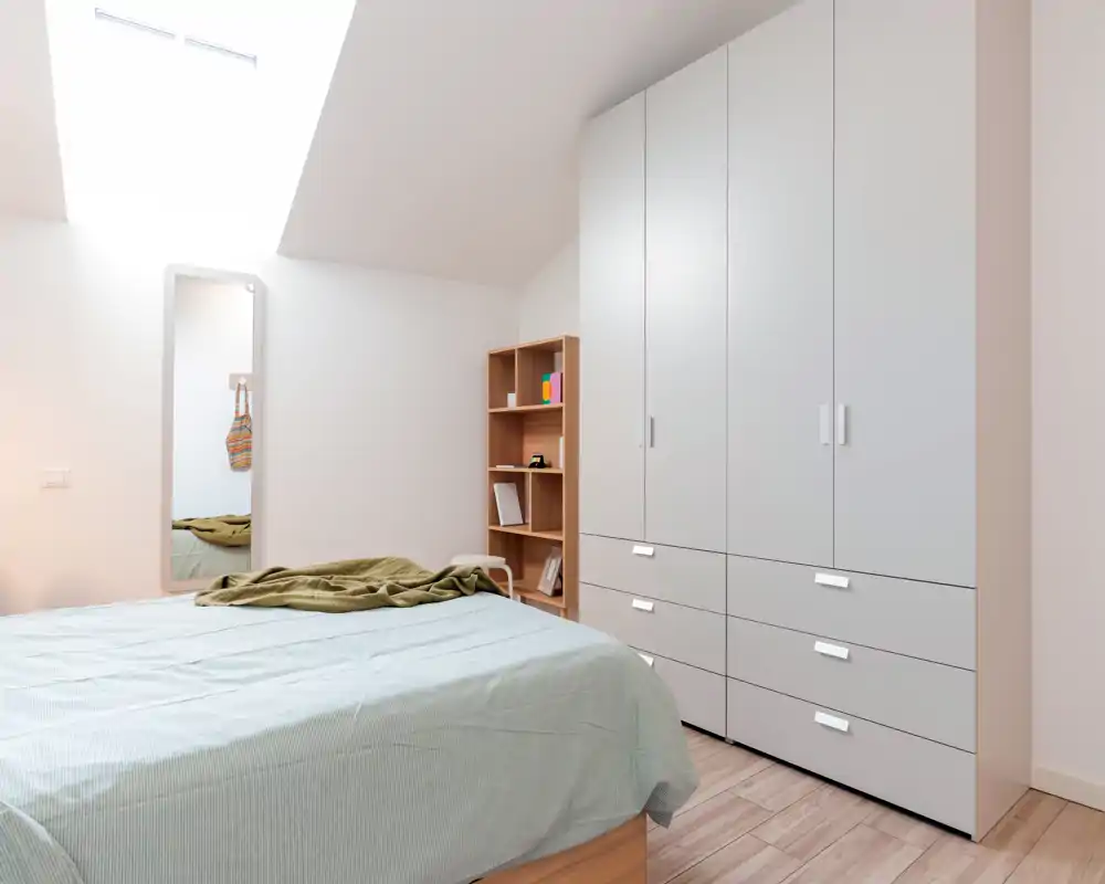 Bright, minimalist bedroom with a large bed, skylight and built-in wardrobe; calm neutral tones and tidy linens create a peaceful sleeping space.