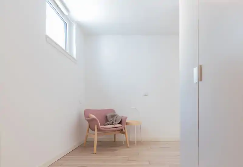 Bright, minimal living corner with a blush armchair, small side table and soft textiles — a calm reading nook bathed in natural light.