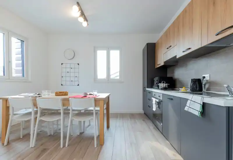 Bright modern open kitchen with integrated gray cabinets, wood upper cupboards and a wooden dining table with four chairs, ideal for compact apartments.