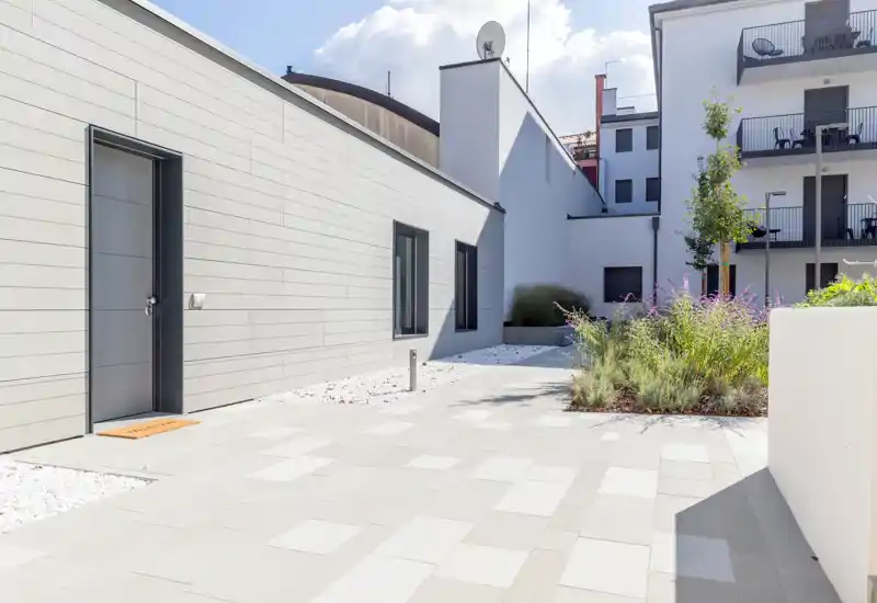 Modern paved courtyard with planted borders and building facade; bright and well maintained outdoor space ideal for short-term rentals.