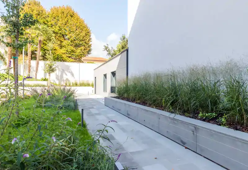 Bright landscaped outdoor walkway with paved path, raised planters and ornamental grasses; a calm private garden/terrace area ideal for a modern rental.