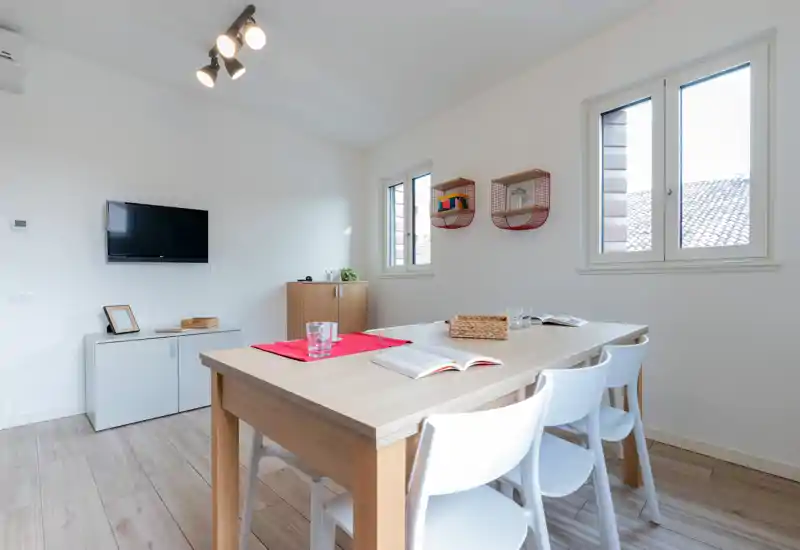 Bright, modern dining area with a light wood table and white chairs, natural light from two windows, and simple decorative details for a clean, welcoming space.
