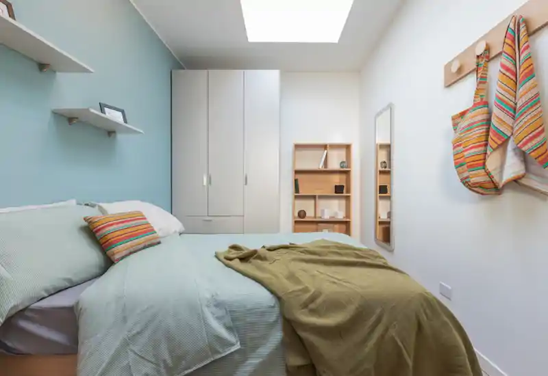 Bright, well-styled bedroom with a large bed, soft linens and a skylight providing natural light; built-in wardrobe and shelving create practical storage.