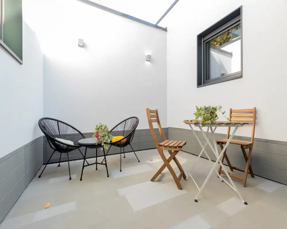 Terraza privada y luminosa con mobiliario moderno: dos sillas de estilo tejido con mesita redonda y un juego de bistró plegable de madera, ideal para café por la mañana o relajarse.