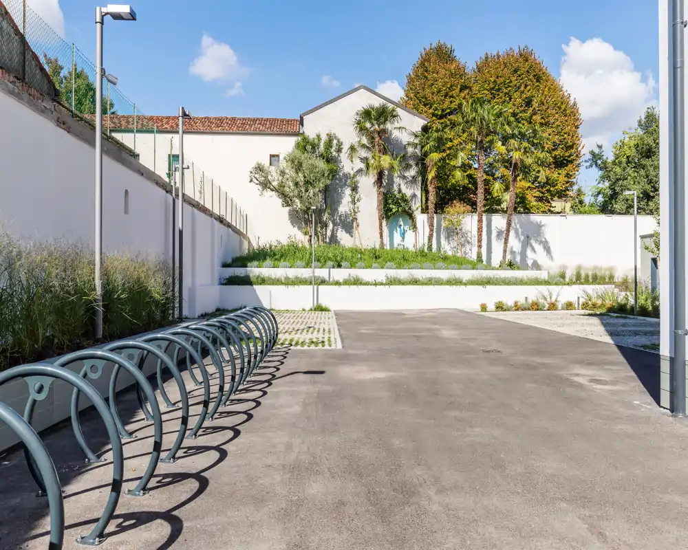 Patio exterior soleado con soporte para bicicletas, zona pavimentada y parterres elevados — ideal como espacio exterior comunitario.