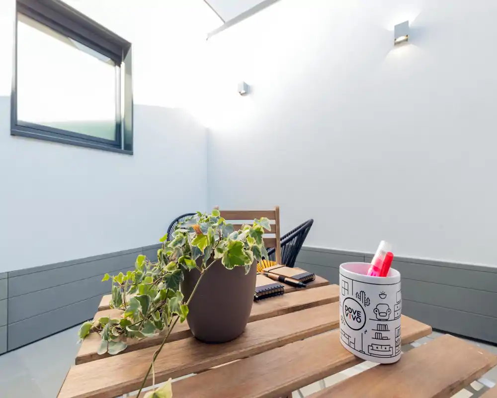 Pequeña terraza privada con mesa de madera, planta en maceta y asientos informales — espacio exterior luminoso, ideal para tomar un café por la mañana o trabajar ligeramente.