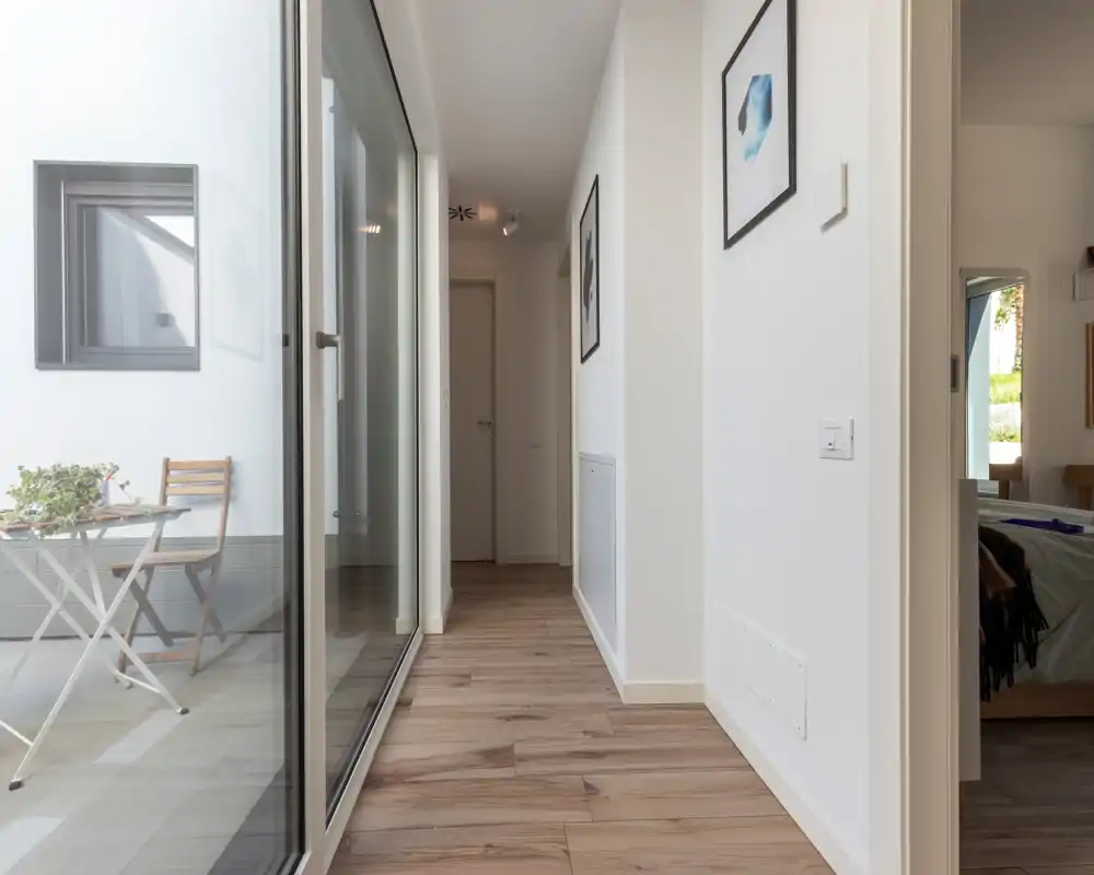 Entrada/pasillo moderno y luminoso con suelo de madera y gran pared de cristal que da a un pequeño patio; decoración minimalista y cuadros que crean un ambiente limpio y acogedor.