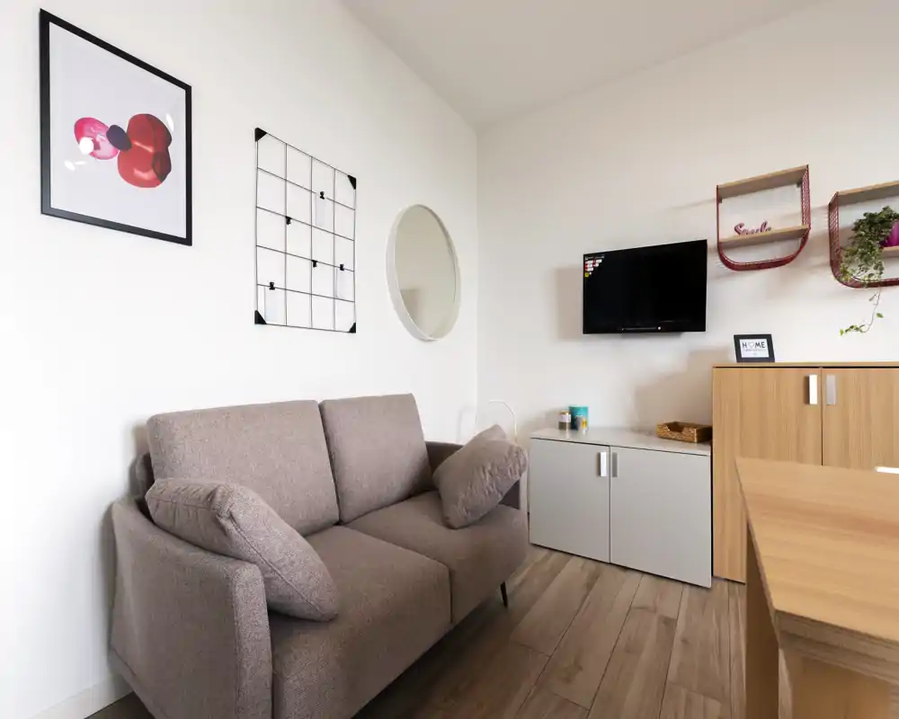 Sala de estar moderna y luminosa con sofá de dos plazas, televisor en la pared y almacenamiento minimalista: ideal para relajarse en un piso compacto.