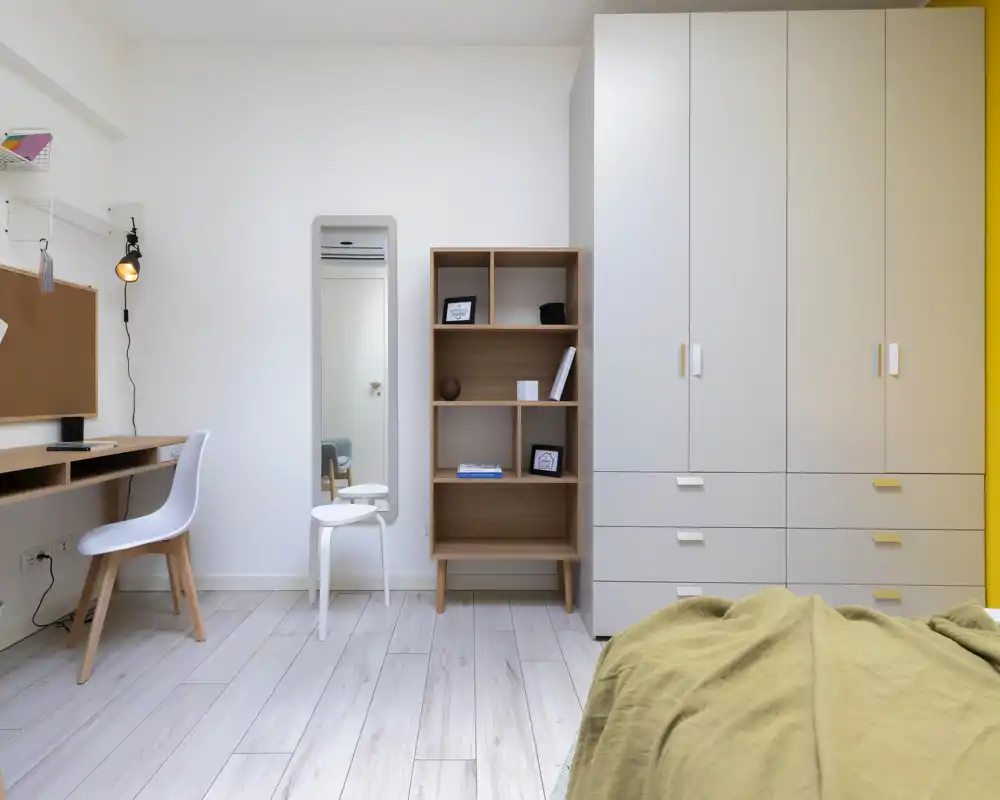 Coin chambre lumineux et minimaliste avec lit partiellement visible, grand placard, étagère et petit bureau — parfait pour une personne ou un étudiant.