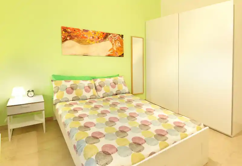 Camera da letto doppia luminosa e ben arredata con biancheria colorata, comodino e grande armadio — perfetta per annunci che vogliono enfatizzare un arredo allegro e spazio di deposito.