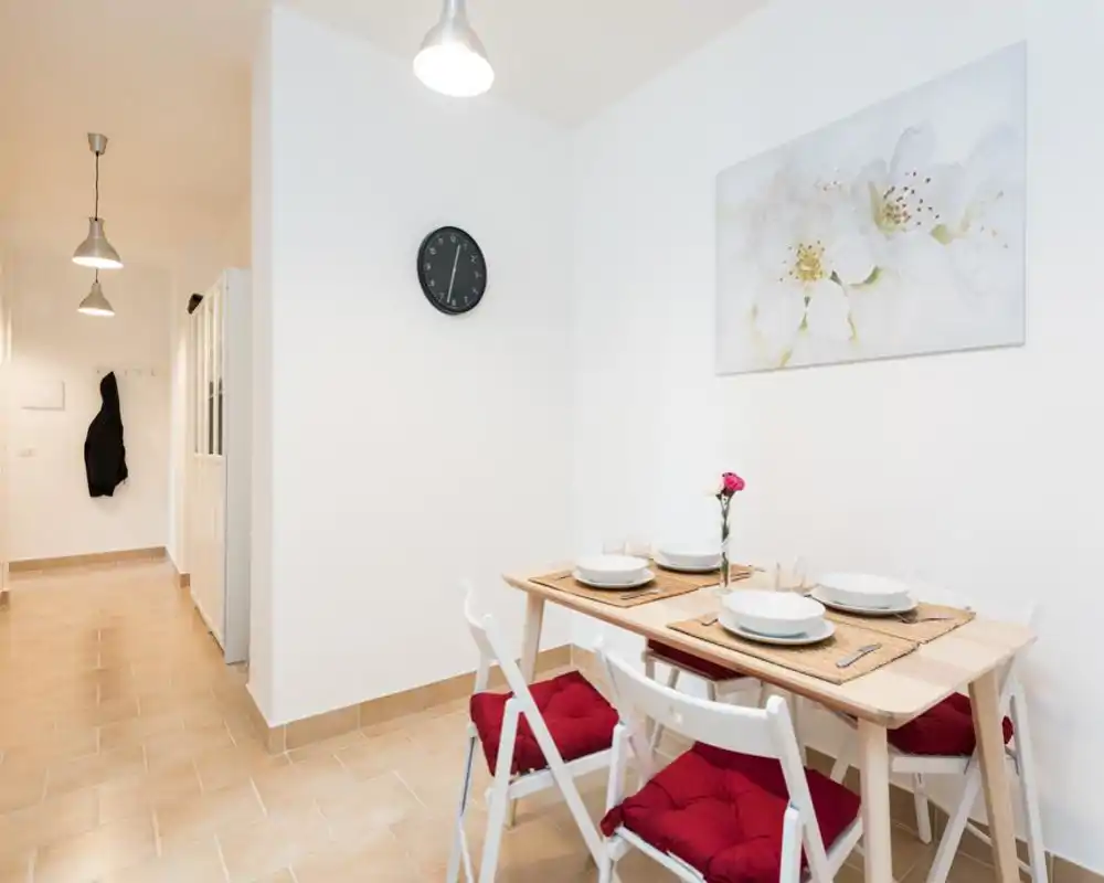 Bright, minimalist dining corner with a wooden table set for four, red seat cushions and simple wall art — ideal for small apartment listings.
