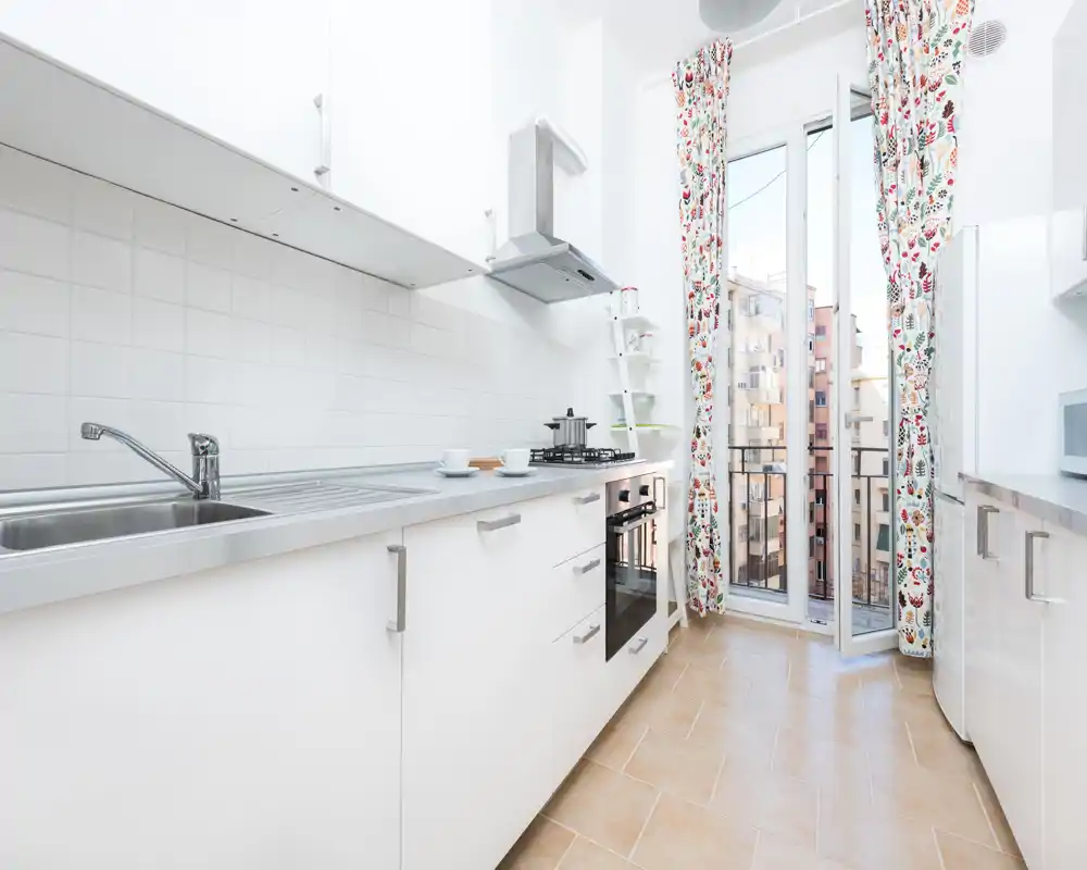 Bright modern kitchen with white cabinets, stainless sink, gas hob and an open balcony door that fills the room with natural light.