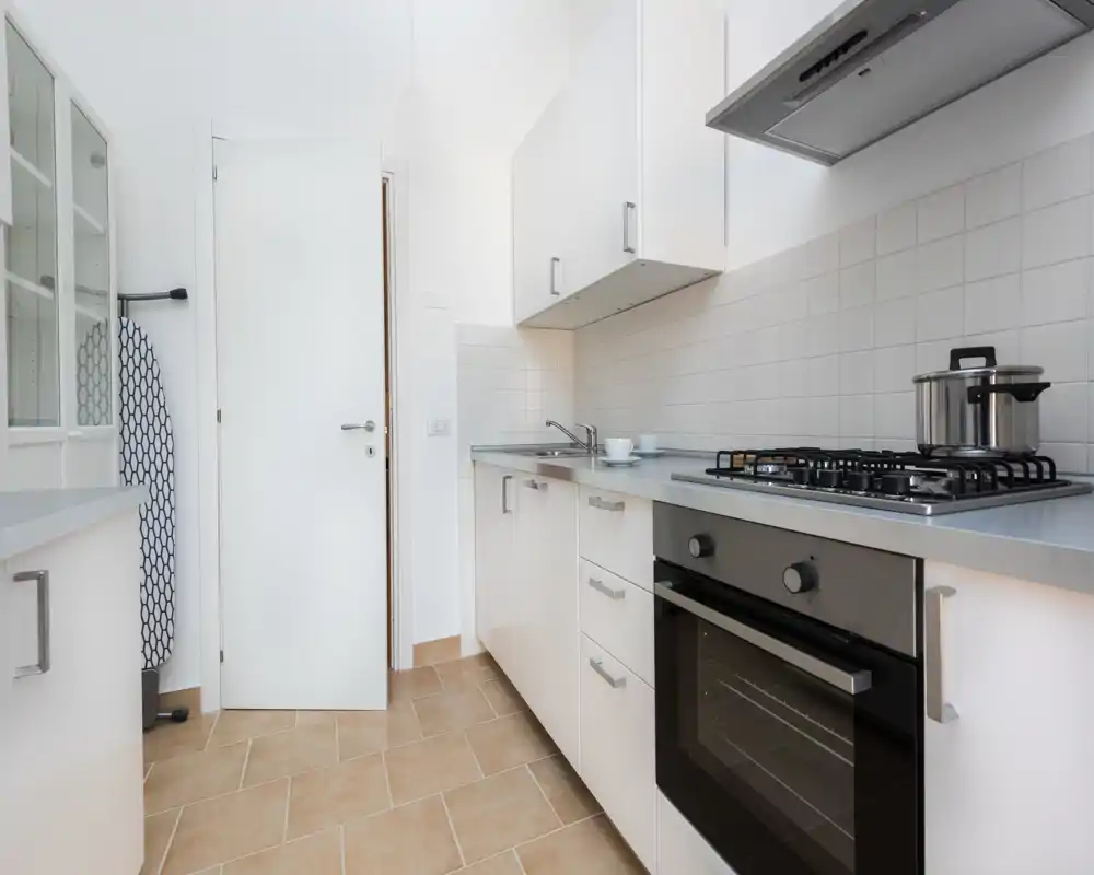 Bright, modern galley kitchen with white cabinets, stainless gas hob and built-in oven; clean minimal styling and practical workspace.