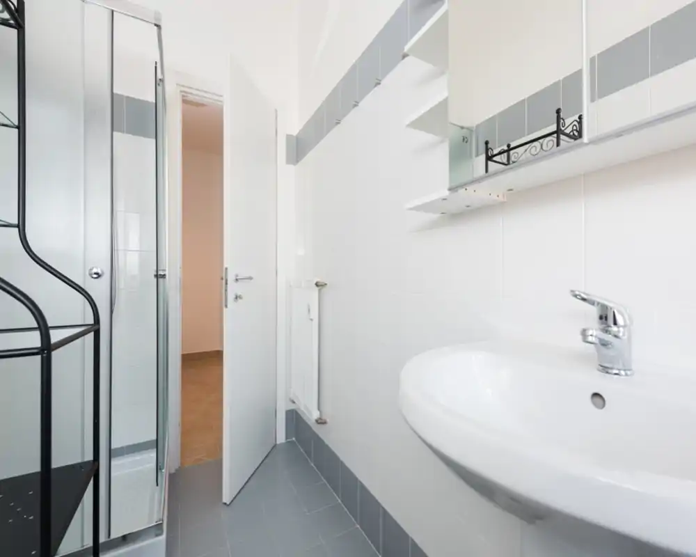 Clean, modern bathroom with a wall-mounted sink, mirrored cabinet and a corner shower cubicle. Neutral white and grey tiles give a fresh, minimal look.
