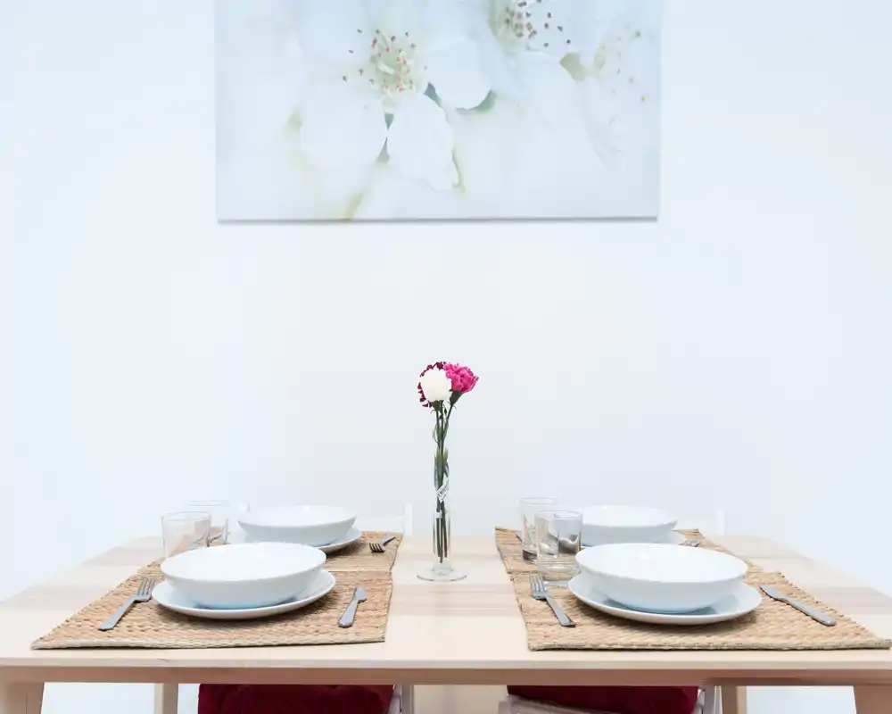 Bright, minimalist dining area with a set table for four, woven placemats and a single-stem vase creating a calm, contemporary atmosphere.