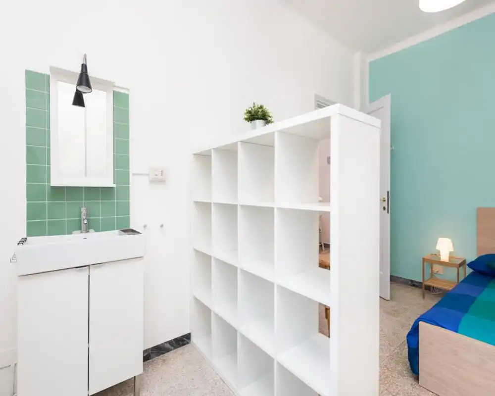 Bright, modern bedroom corner with a visible single bed, a bedside table and a white shelving divider; fresh mint accent wall and a small sink area add functional convenience.