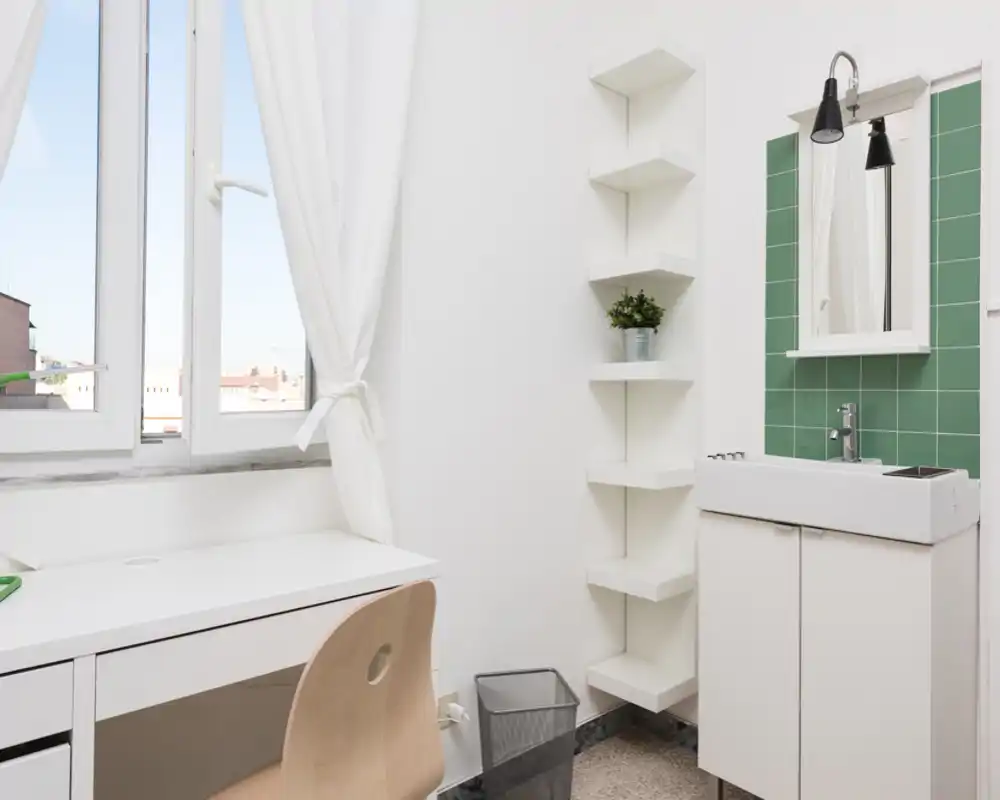 Bright, minimal corner with a white sink, green tiled splashback and a desk by the window — compact and clean wash area ideal for a small apartment.